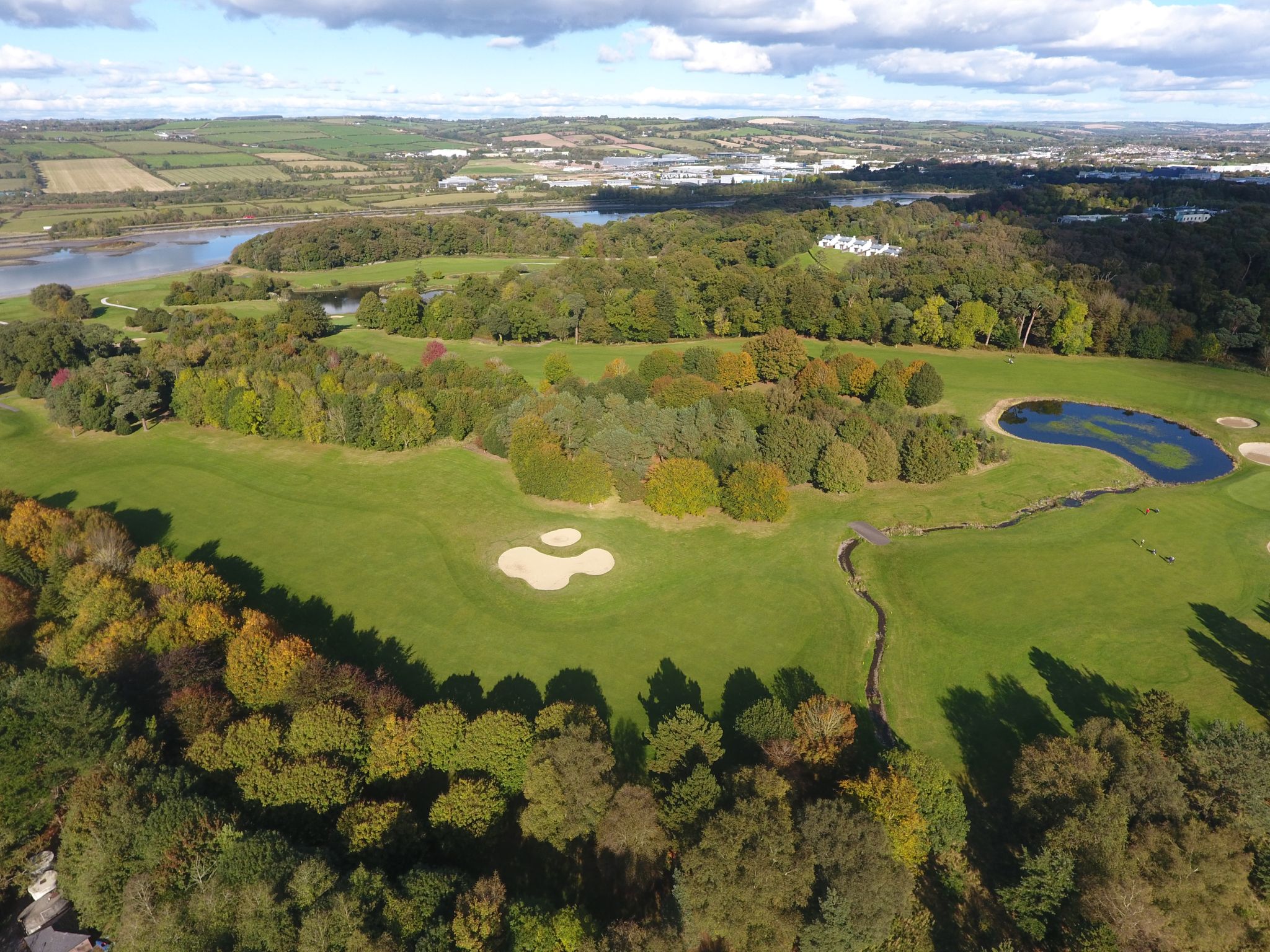 Drone image of golf course with bunker, lake and trees changing colour into autumn
