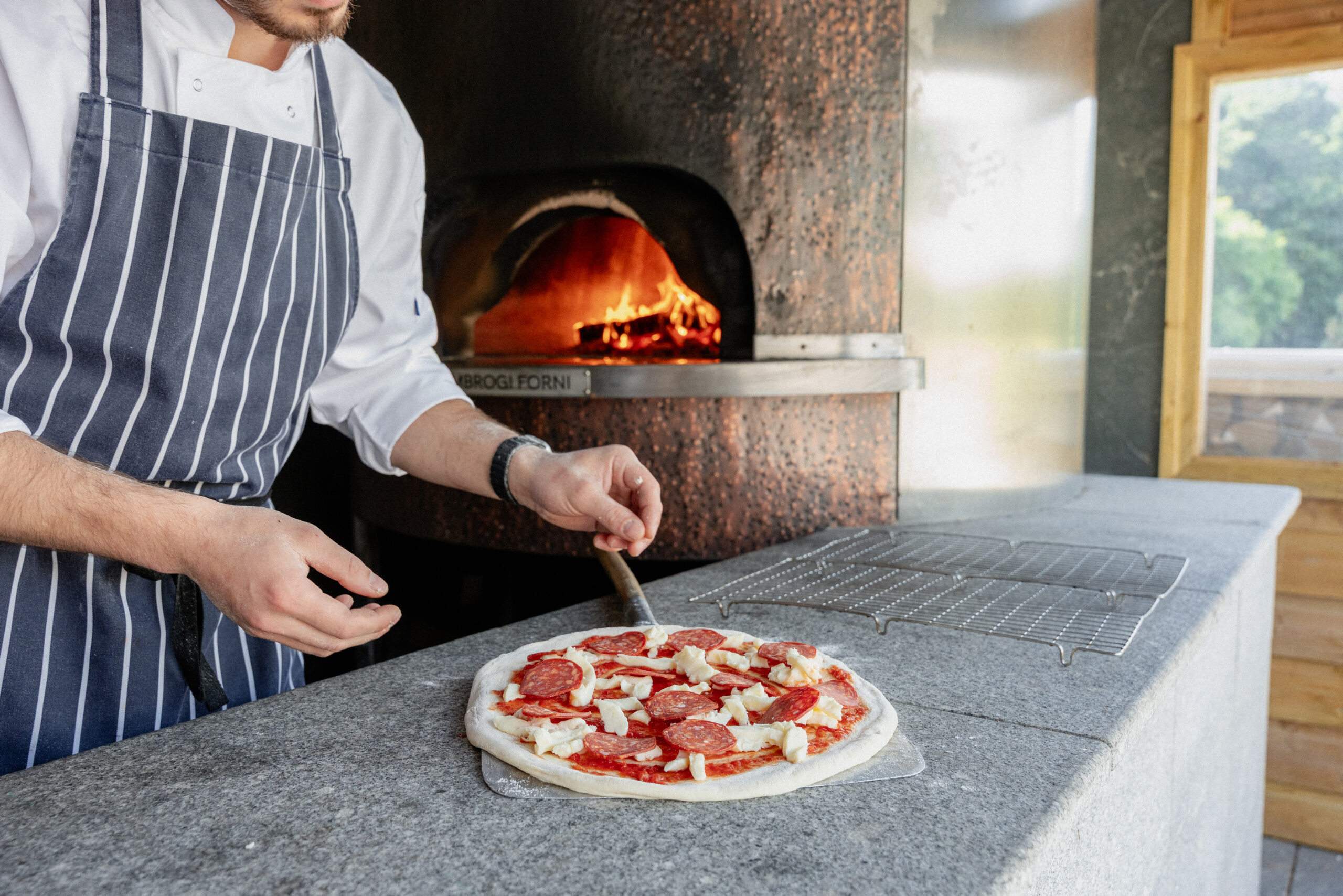 Chef preparing a pizza to cook in front of the wood fire pizza oven at The Clubhouse