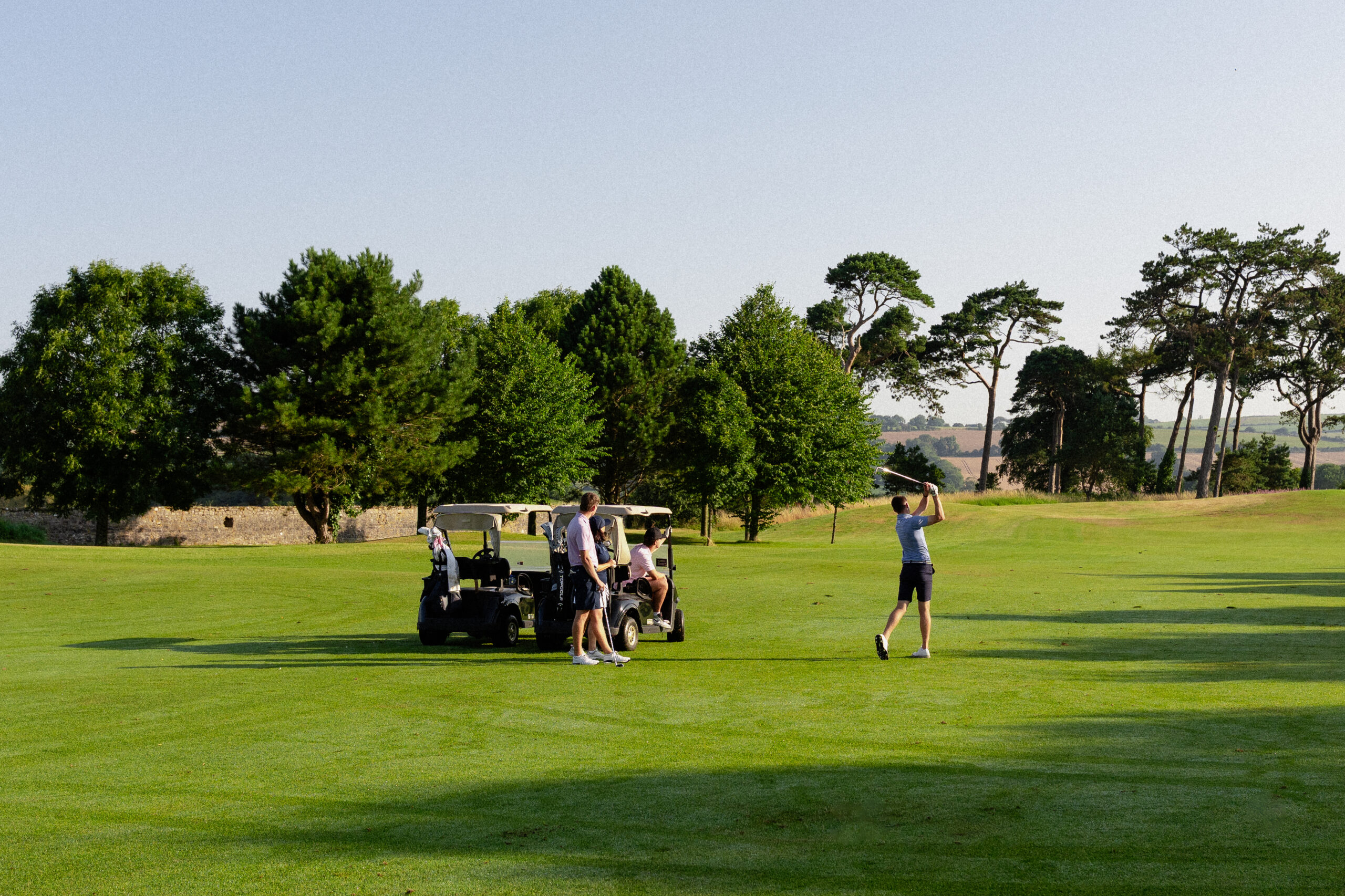 Image of golfer alongside buggies playing an iron into the green