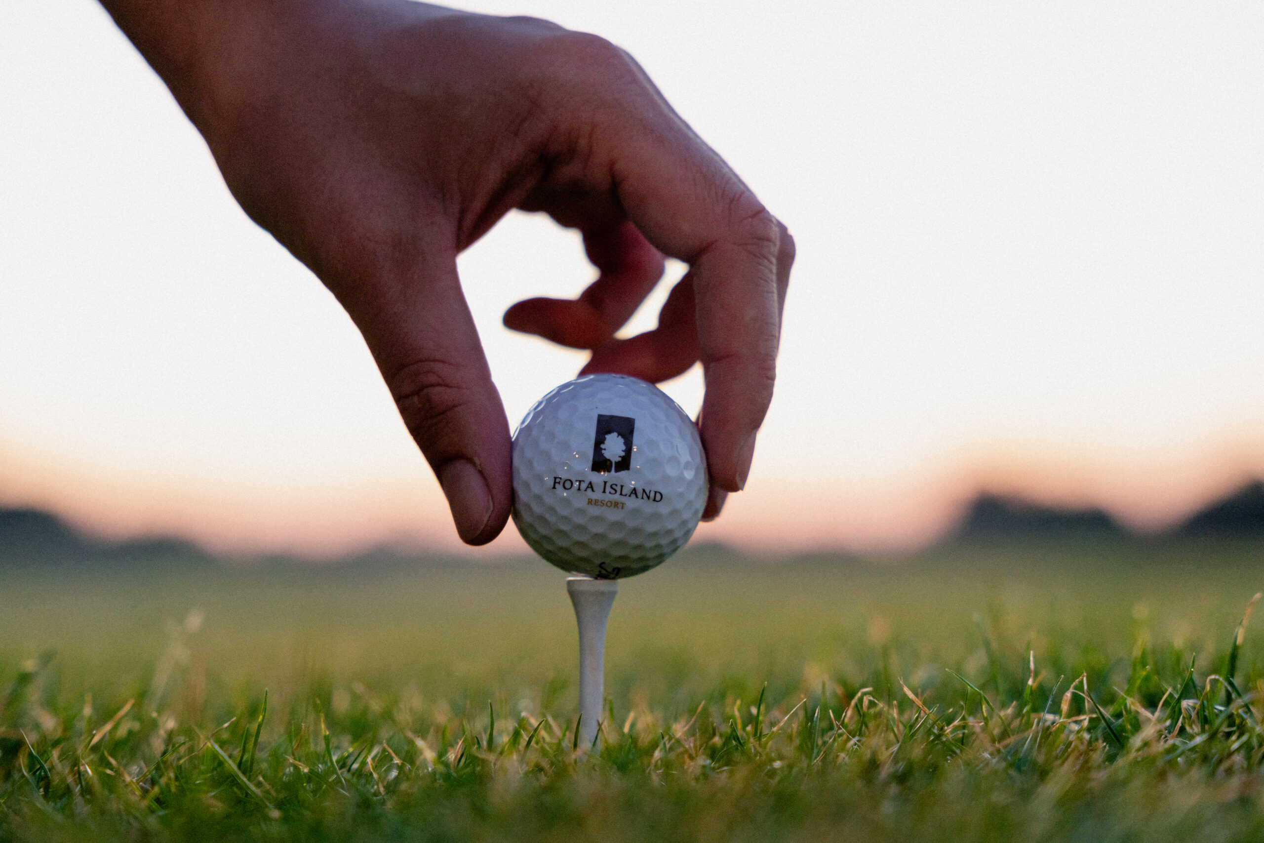 Golf ball upclose being placed on tee with Fota Island Resort logo at sunset