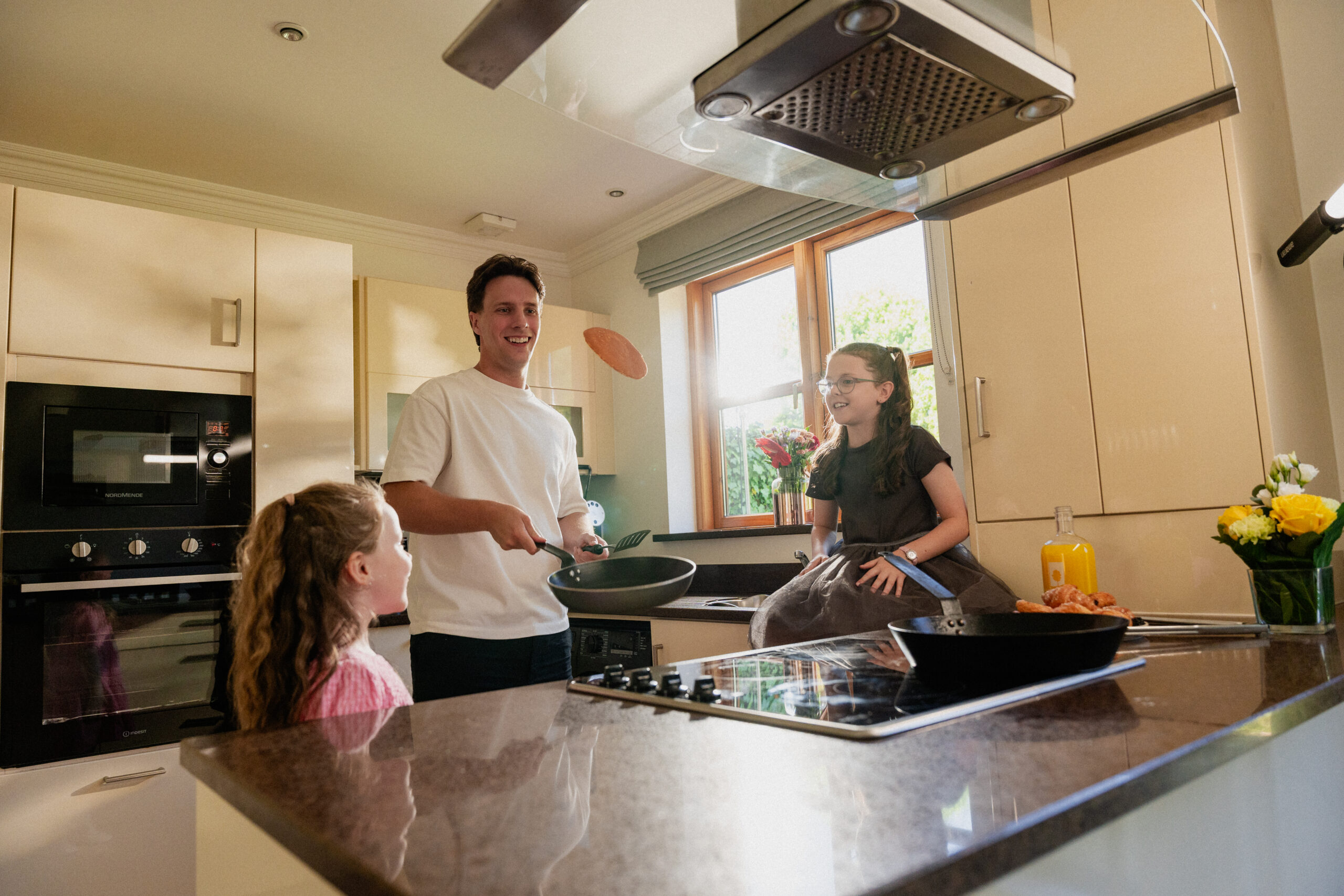 Dad flipping pancake in the kitchen of a self-catering lodge with two children watching