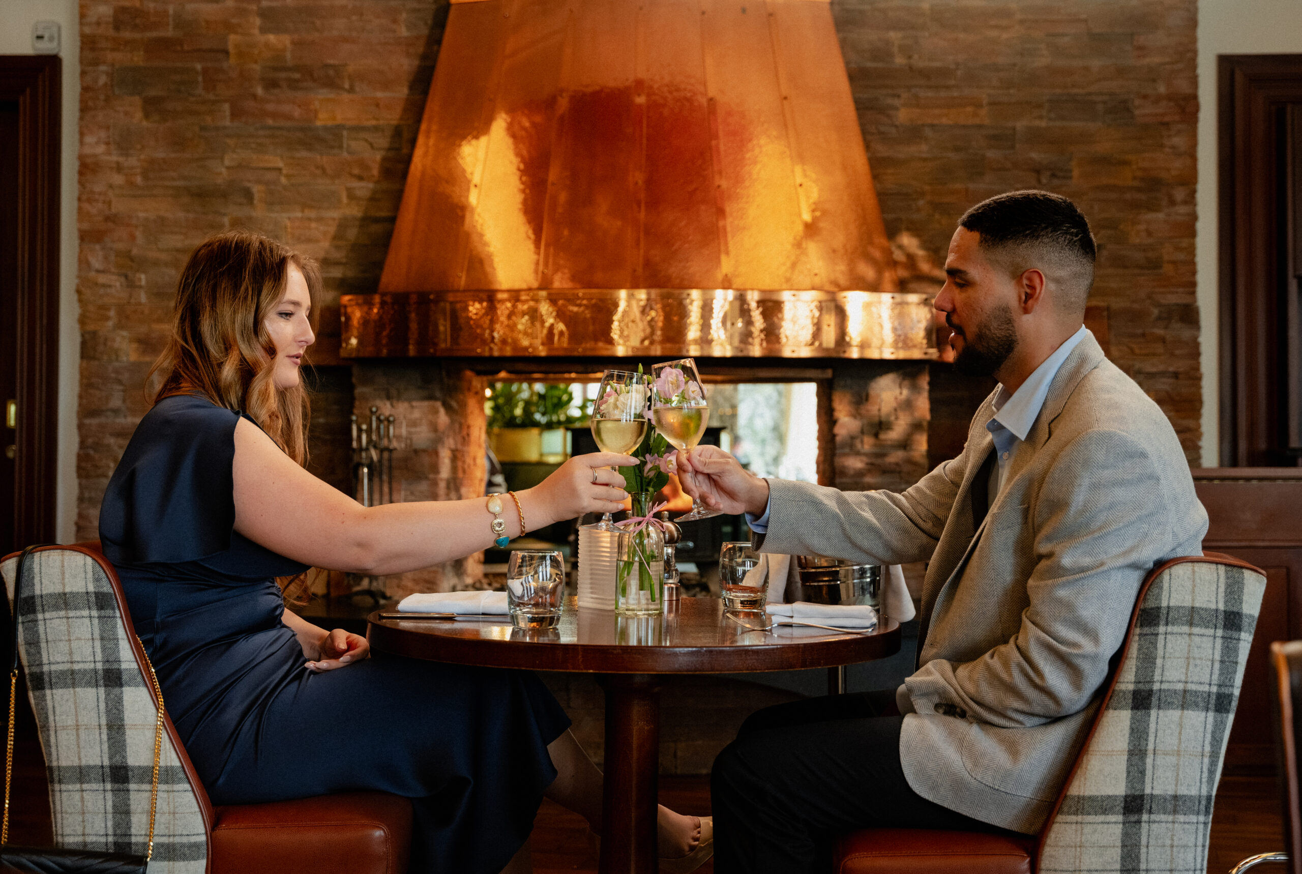 Couple dining in front of the fire at The Amber Lounge raising a glass to one another