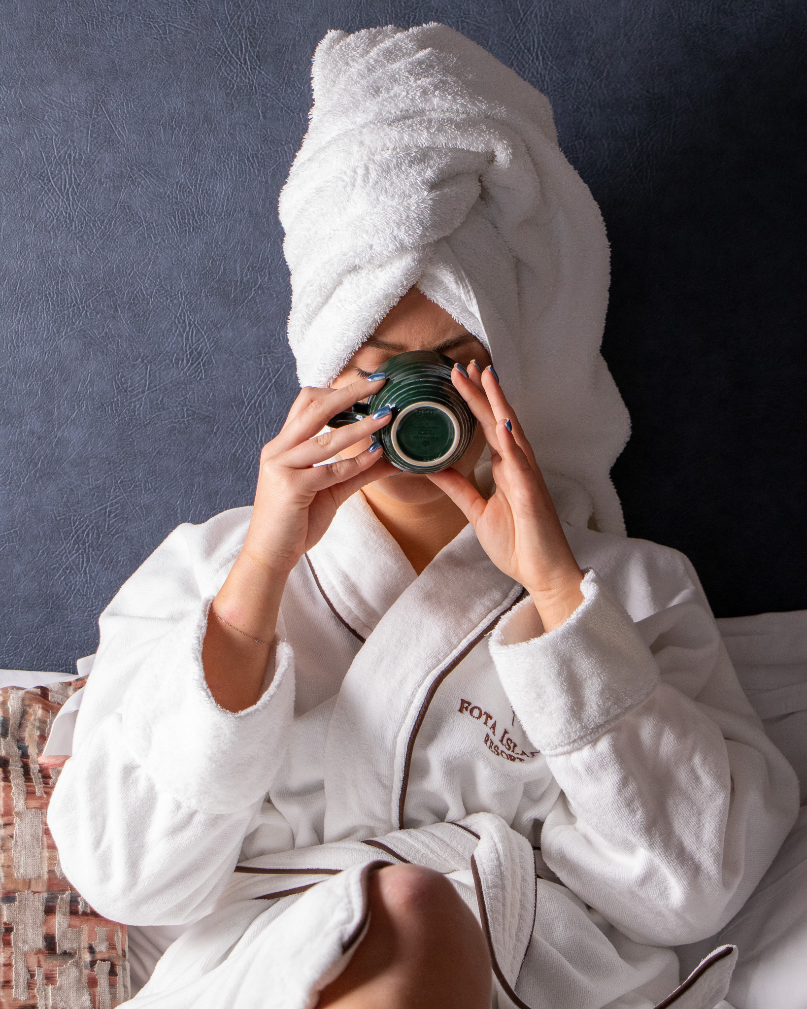 lady on bed in robe and head towel drinking from cup