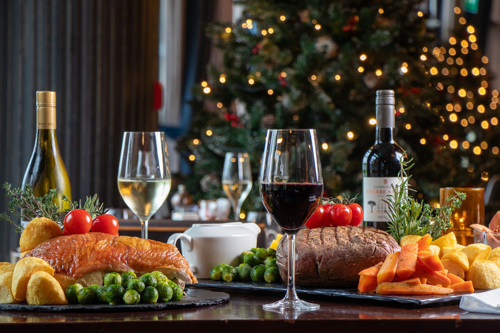 Sunday lunch spread on table with wines and Christmas tree in the background