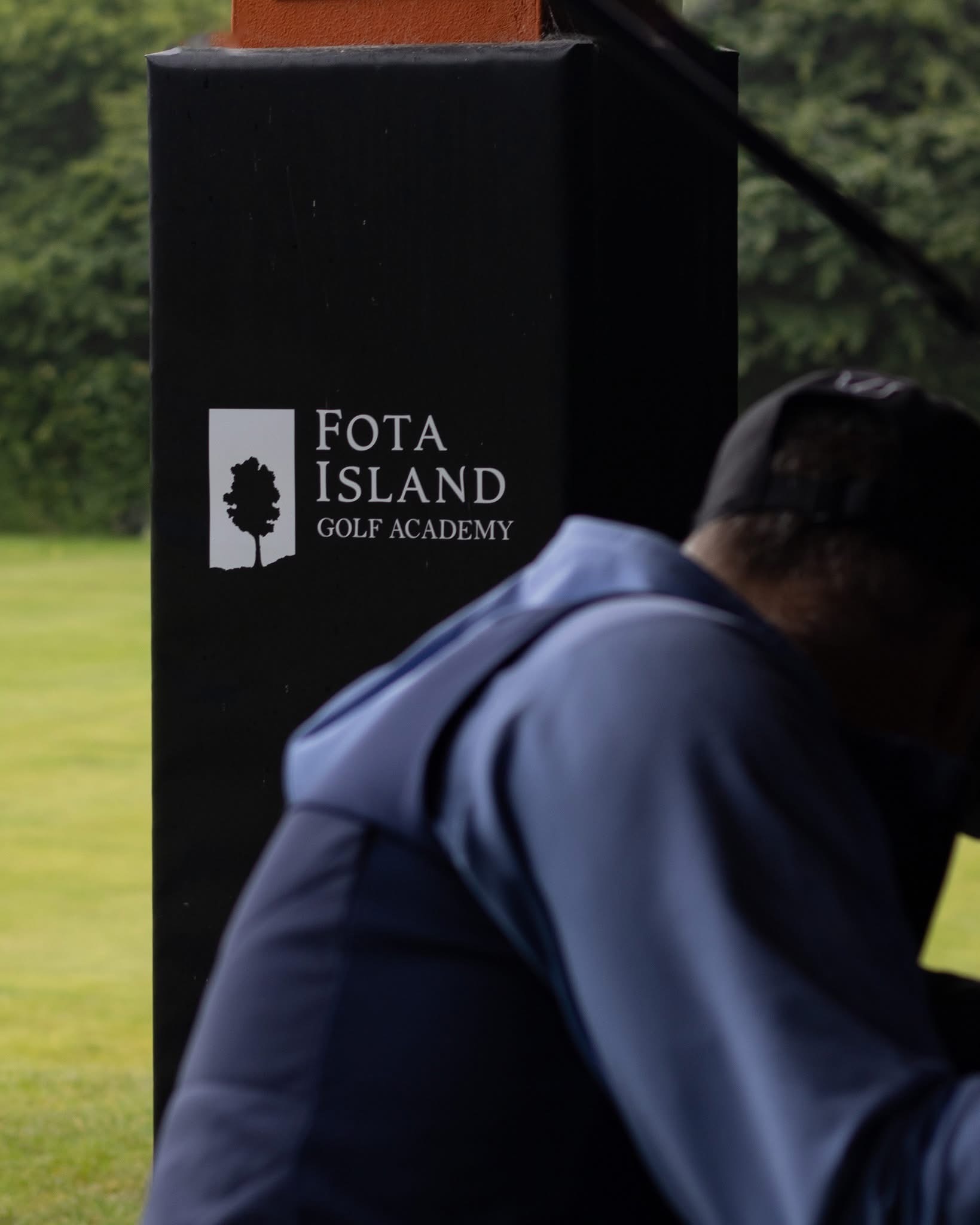 Golfer backswing with focus on Fota Island Golf Academy on wall behind.